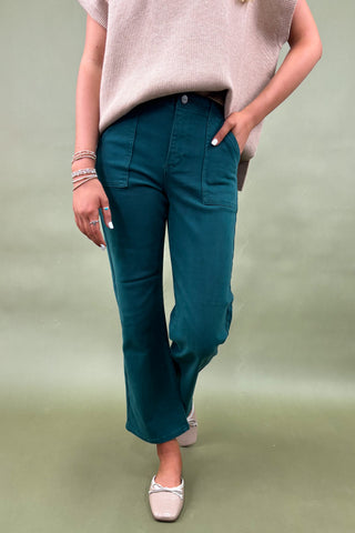 Person wearing teal pants and a beige sweater on a plain background