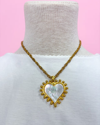 Woman wearing a gold necklace with a heart-shaped pendant on a white background