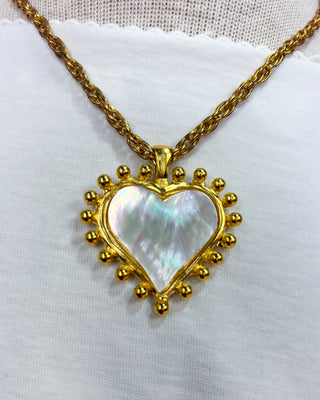 Woman wearing a gold necklace with a heart-shaped pendant on a white background