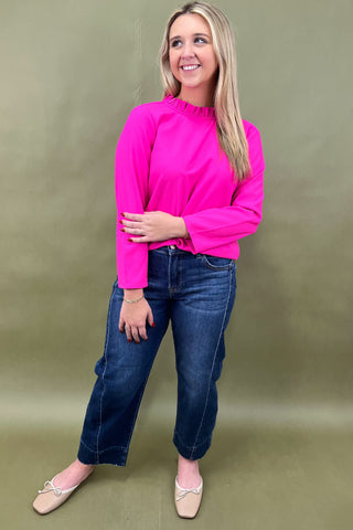 Woman wearing a bright pink top and blue jeans against a green background