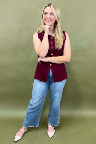 Woman wearing a burgundy sleeveless top and blue jeans against a green background