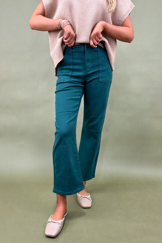 Person wearing teal pants and a light pink top on a green background