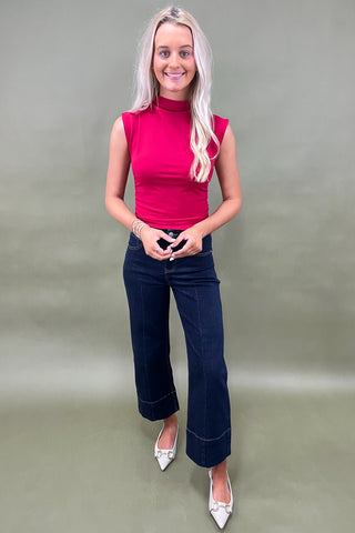 Woman wearing a pink sleeveless top and dark blue jeans against a green background