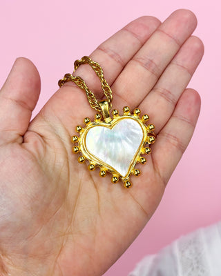 Woman wearing a gold necklace with a heart-shaped pendant on a white background