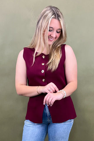 Woman wearing a burgundy sleeveless top with buttons against a green background