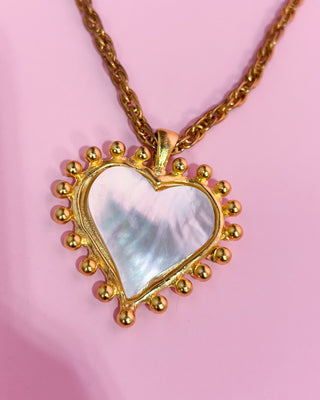 Woman wearing a gold necklace with a heart-shaped pendant on a white background