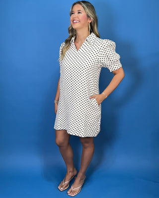 Woman modeling an ivory polka dot puff sleeve mini dress with a button-front design.