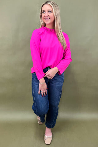 Woman wearing a bright pink top and blue jeans against a green background