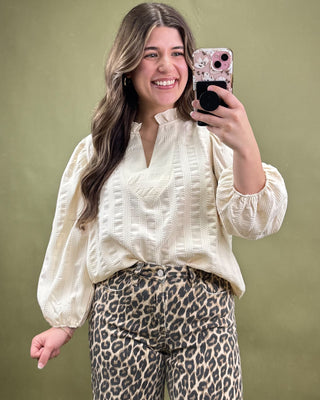 Woman taking a mirror selfie wearing a cream blouse and leopard print pants against a green background