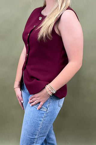 Person wearing a burgundy sleeveless top and blue jeans against a green background