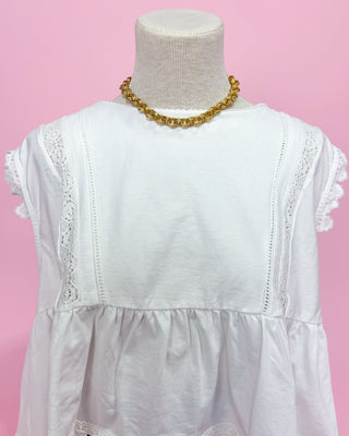 White lace-trimmed dress on a mannequin with a pink background