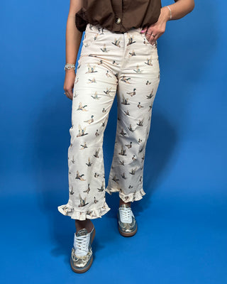 A person wearing cream-colored cropped pants with a brown and gray duck print, paired with a brown top and metallic silver sneakers