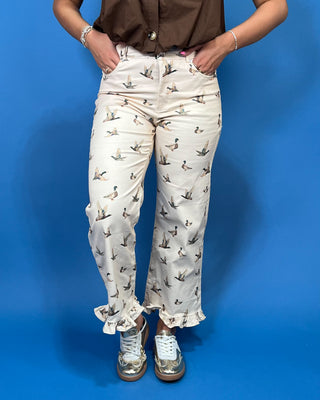 A person wearing cream-colored cropped pants with a brown and gray duck print, paired with a brown top and metallic silver sneakers