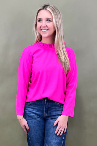 Woman wearing a bright pink top and blue jeans against a plain background