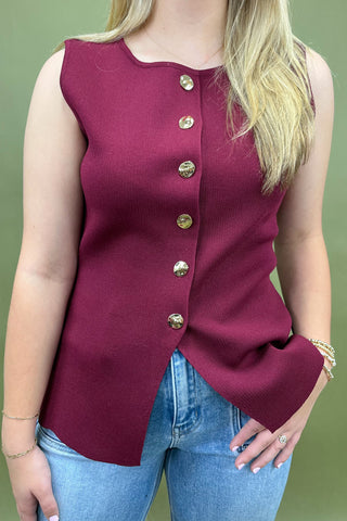 Maroon sleeveless top with gold buttons worn by a person on a green background