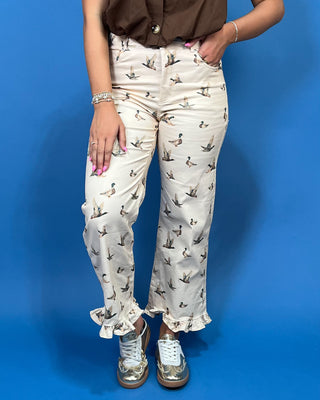 A person wearing cream-colored wide-leg pants with a brown duck print, paired with a brown shirt and metallic silver sneakers