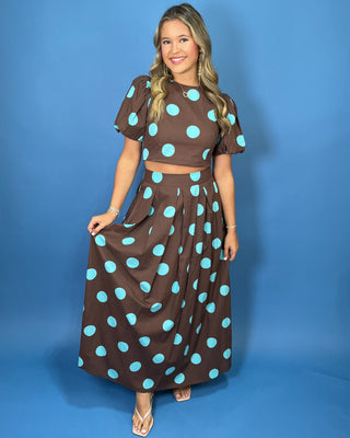 Woman modeling a brown and turquoise polka dot puff sleeve crop top with a matching pleated maxi skirt.