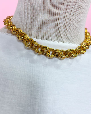 Gold chain necklace on a mannequin with a pink and white background
