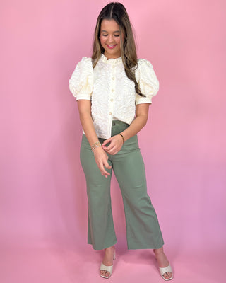 Woman wearing a white blouse and green pants against a pink background