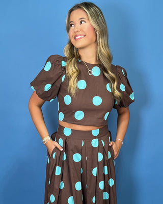 Woman modeling a brown and turquoise polka dot puff sleeve crop top with a matching pleated maxi skirt.