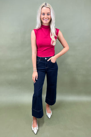 Woman wearing a pink sleeveless top and dark blue jeans against a green background