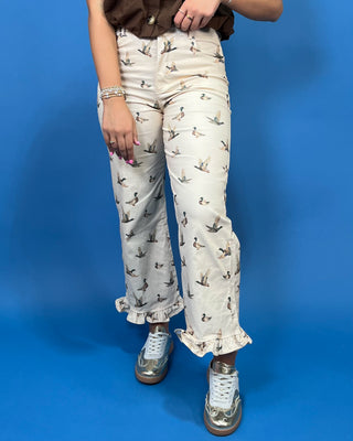A person wearing cream-colored cropped pants with a brown and gray duck print, paired with a brown top and metallic silver sneakers