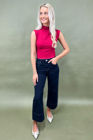 Woman wearing a pink sleeveless top and dark blue jeans against a green background