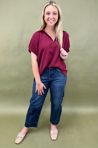 Woman wearing a maroon shirt and blue jeans against a green background