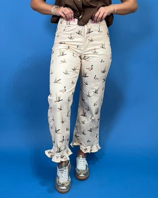 A person wearing cream-colored pants with a brown and black bird print, styled with a brown top and metallic sneakers