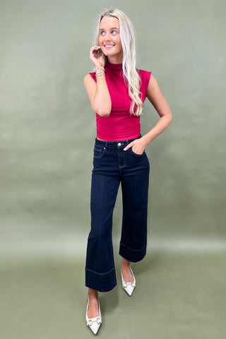Woman wearing a pink top and dark blue jeans against a plain background
