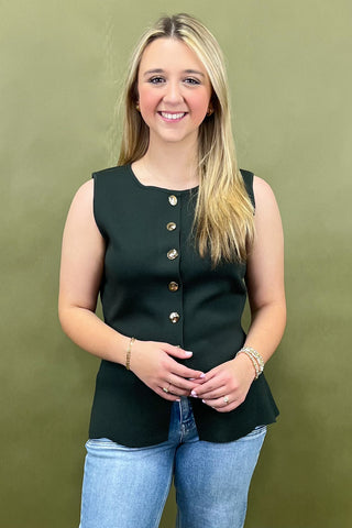 Woman wearing a black sleeveless top with gold buttons against a green background