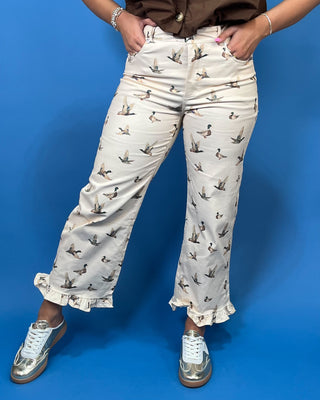 A person wearing cream-colored cropped pants with a brown and gray duck print, paired with a brown top and metallic silver sneakers