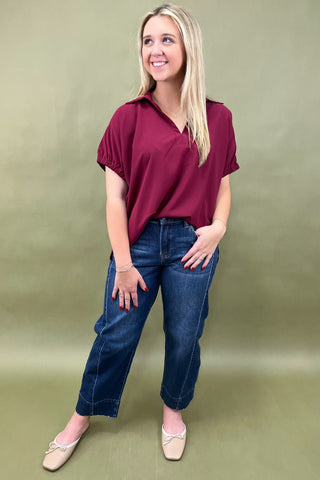 Woman wearing a maroon top and blue jeans against a green background