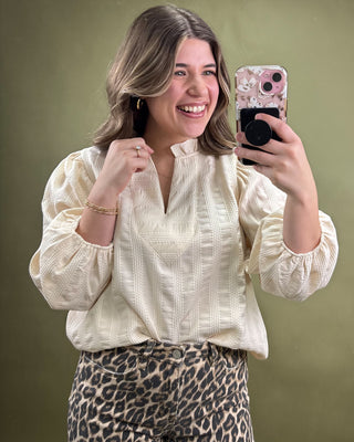 Woman taking a selfie wearing a white blouse and leopard print pants against a green background