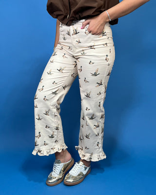 A person wearing cream-colored cropped pants with a repeating duck print, paired with metallic silver sneakers