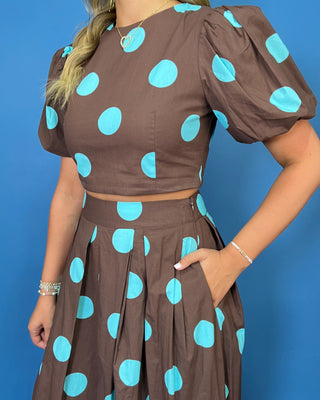 Woman modeling a brown and turquoise polka dot puff sleeve crop top with a matching pleated maxi skirt.