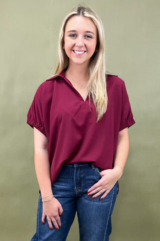 Woman wearing a burgundy blouse and blue jeans against a green background