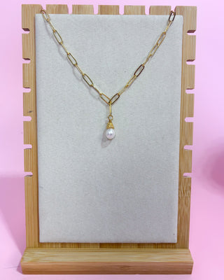 Gold necklace with a pearl pendant on a wooden stand against a pink background