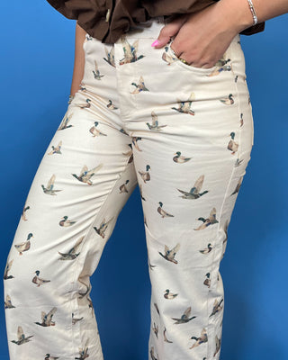 A person wearing cream-colored pants with an all-over printed pattern of flying mallards, paired with a brown top