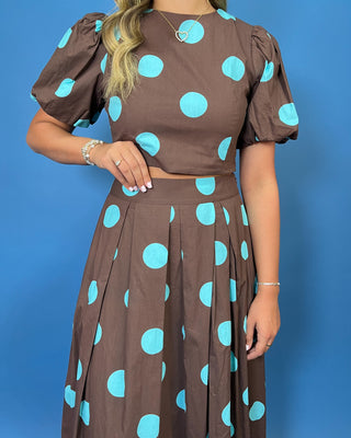 Woman modeling a brown and turquoise polka dot puff sleeve crop top with a matching pleated maxi skirt.