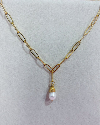 Gold chain necklace with a pearl pendant on a light gray background