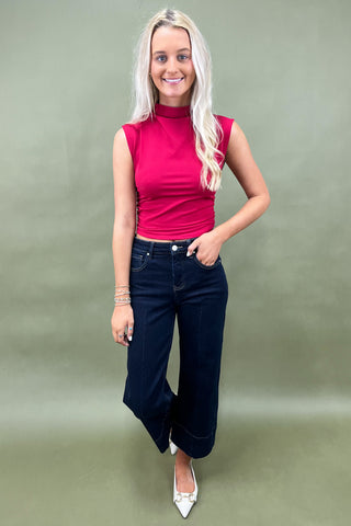 Woman wearing a pink sleeveless top and dark blue jeans against a green background