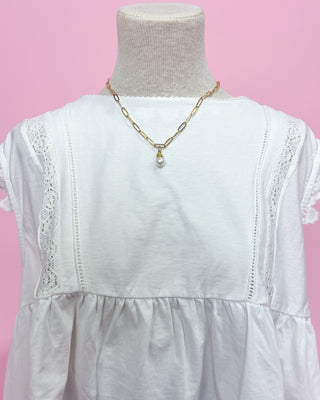 White lace top on a mannequin with a gold necklace against a pink background