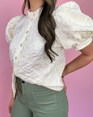 Woman wearing a white textured blouse with puff sleeves against a pink background