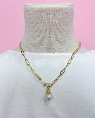 Gold chain necklace with a pearl pendant on a mannequin against a pink background