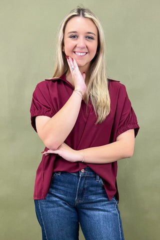 Woman wearing a maroon shirt and blue jeans against a green background