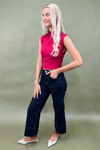 Woman wearing a pink top and dark blue jeans against a plain background