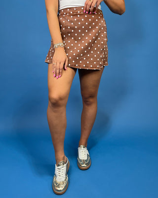 A person wearing a brown mini skirt with a white polka dot pattern, paired with metallic silver sneakers