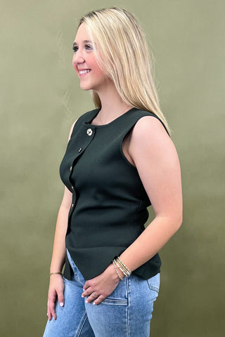 Woman wearing a black sleeveless top and blue jeans against a green background