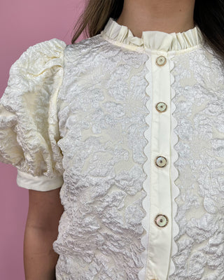 Close-up of a white lace blouse with ruffled sleeves against a pink background